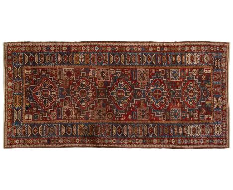 An antique red ground Shirvan carpet with five stepped diamond lozenges on a central pole, within stylized geometric borders,