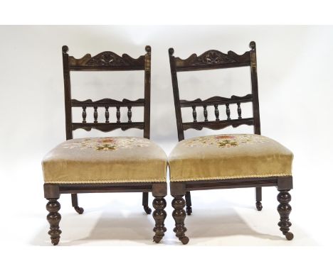 A pair of Edwardian nursing chairs with bobbin turned splats above a over stuffed seats, raised on turned legs with casters