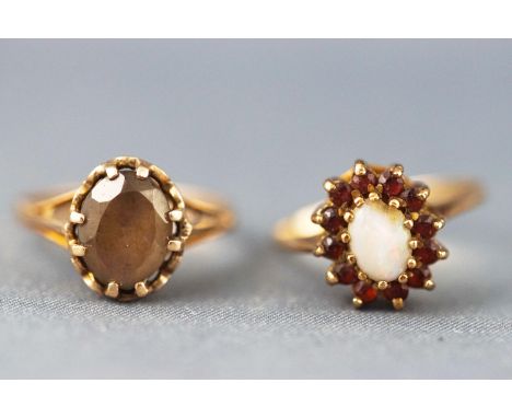 A yellow metal opal and garnet cluster ring together with a yellow metal single stone quartz ring. Both hallmarked 9ct gold. 