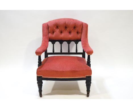 A Victorian nursing chair with button back and upholstered arms, on an ebonised frame with turned tapering legs