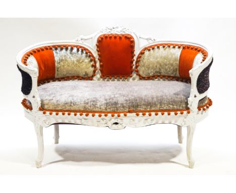 A small painted carved wood sofa with curved ends, the back set with three upholstered panels under a central floral motif.  