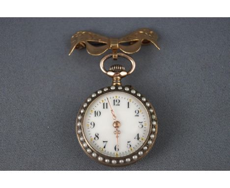 A open face fob watch with blue enamel finish and seed pearls fixed to a 9ct gold bow brooch. White ceramic dial with rose gi