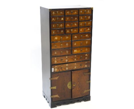 An Oriental hardwood cabinet with three tiers of twenty drawers over a two door cupboard, the drawer fronts decorated with in