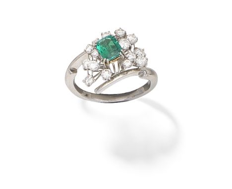 EMERALD AND DIAMOND DRESS RINGThe step-cut emerald within a spray of brilliant-cut diamonds, obliquely set between crossover 