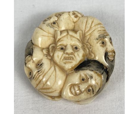 A bone netsuke carved in the form of 9 different faces. With slits to side panels and central hole carved with a floral borde