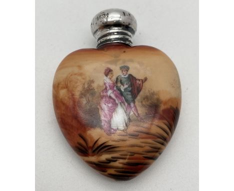 An early 20th century ceramic scent bottle with hallmarked silver screw top lid. Heart shaped bottle featuring a lovers scene