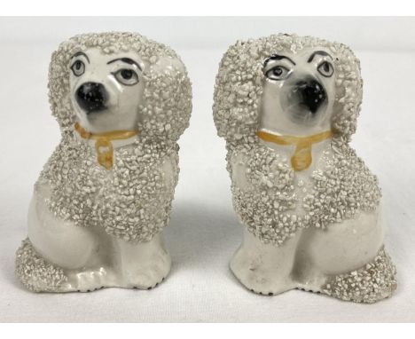 A pair of antique Staffordshire ceramic poodle figurines with hand painted yellow collars. Chip to back of left hand side dog