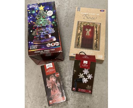 4 boxed Christmas decorations. A large silver light up bow, a snowflake projector, an LED light up Christmas tree with train 