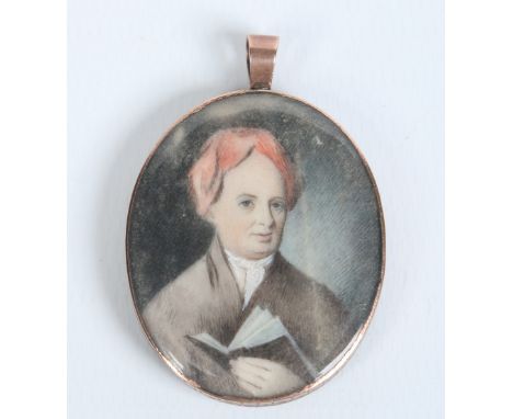 A Georgian mourning pendant in engraved yellow metal mount and set with an ivory portrait miniature of a gentleman reading a 