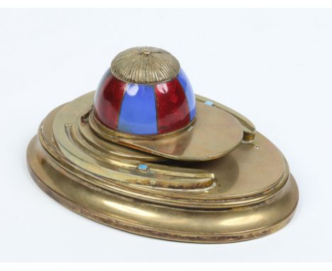 A brass equestrian theme ink well. The hinged cover is formed as a jockeys cap and with red and blue enamel decoration, the o