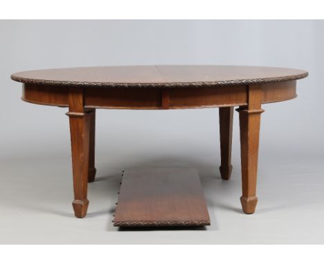 A late Victorian light oak oval wind out dining table raised on square tapering supports and with extra leaf and winding hand