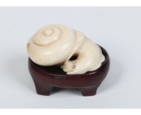 A Japanese carved ivory netsuke on associated carved hardwood plinth. Modelled in the form of a snail. Signed, 4.5cm. Conditi