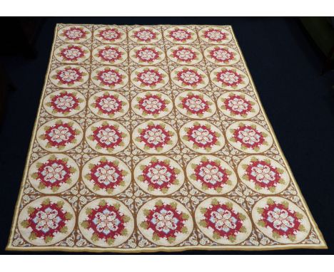 A good hand-stitched tapestry rug: beige ground with a 35-roundel symmetrical design of red, blue and green garlands, (in goo
