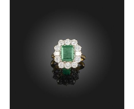 An emerald and diamond ring, of cluster design, set with a step-cut emerald, within a border of brilliant-cut and baguette di