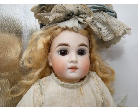 A Belton bisque doll with fixed brown glass eyes, brown feathered brows, closed mouth with slight gap between, original blond