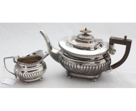 A silver teapot with shaped finial, ebonised handle and half-gadrooned body raised on four bun feet, together with a matching