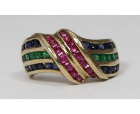 A 9K ruby, sapphire and emerald ring, of cross-over swirl design, channel set, with 10x round-faceted emeralds, 14x rubies an
