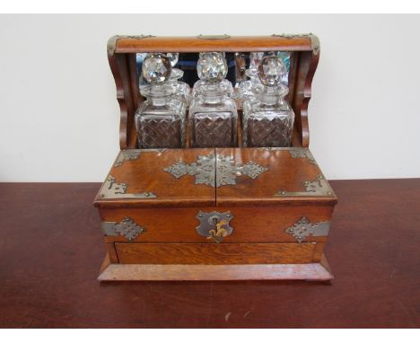 An Edwardian oak three bottle tantalus with lift up flaps opening to reveal a fitted interior and three glasses. Depress butt