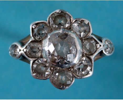 A Victorian diamond cluster ring, the large flowerhead flanked by two old brilliant cut stones, in a white and yellow coloure