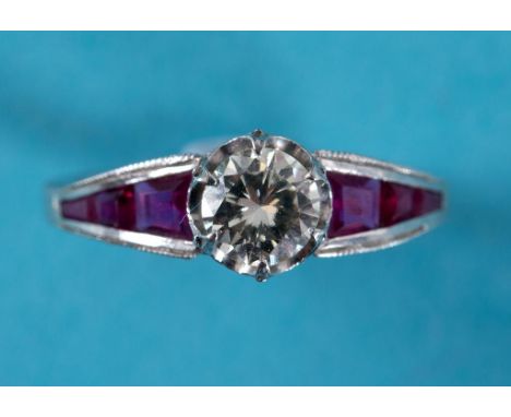 A diamond and ruby ring, the central diamond flanked by ruby set shoulders, the white coloured metal setting set diamonds to 
