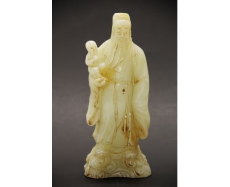 A Chinese carved pale celadon jade figure of a lucky God holding a child while standing on clouds, H. 70cm.