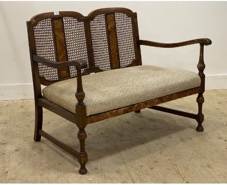 A 1930's walnut two seat sofa, the bergere panelled back over two open arms and a drop in upholstered seat pad, raised on tur