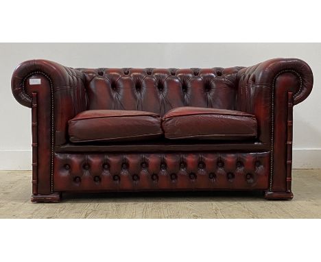 A vintage two seat Chesterfield sofa, upholstered in deep buttoned oxblood red leather, moving on castors. H70cm, W142cm, D80