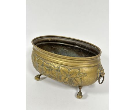 A Edwardian chased oval brass planter with leaf and flower head side panel designs and cast lion mask ring handles to side ra