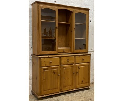 A polished pine dresser, the top section fitted with a open shelf and drawer flanked by two glazed doors enclosing four shelv