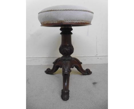 A late Victorian walnut piano stool, the rotating height adjustable seat upholstered in a beige fabric, over a turned and fol