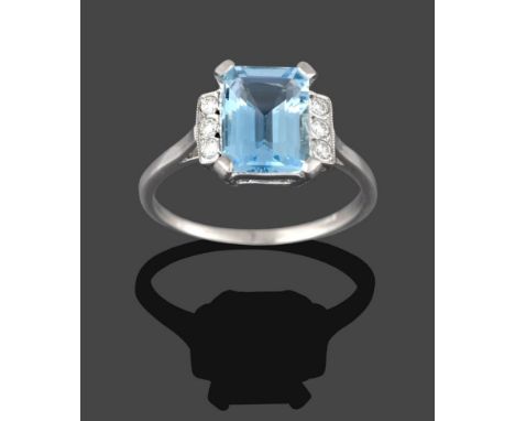 An Aquamarine and Diamond Ring, the emerald-cut aquamarine in white claw settings, flanked by trios of round brilliant cut di