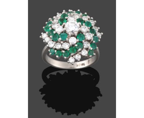 An Emerald and Diamond Cluster Ring, a round brilliant cut diamond within a swirling border of alternate rows of round cut em