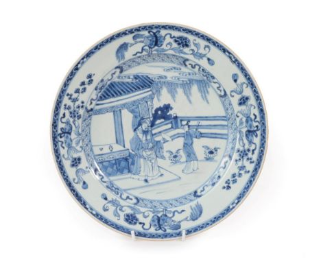 A Chinese Porcelain Dish, Kangxi, painted in underglaze blue with figures in a fenced garden within a foliate border 23cm dia