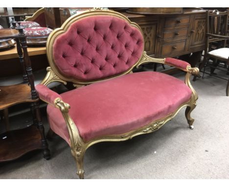 A red button back two seater sofa with a craved giltwood frame, approx 123cm x 97cm x 65cm.