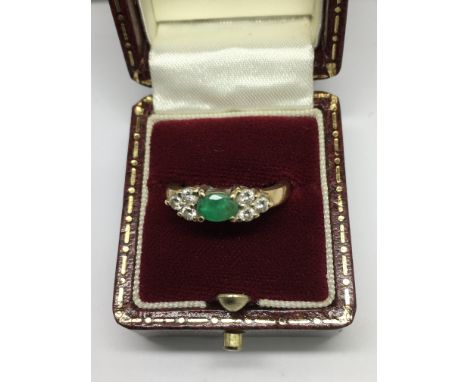 A gold ring set with a central emerald flanked by diamond set shoulders.Approx size K