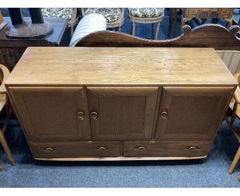 An Ercol style light elm sideboard, with three panel doors above two short drawers, on castors, 129cm wide
