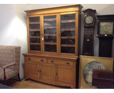 A golden oak bookcase cabinet c. 1900, the upper section with moulded cornice above three glazed doors enclosing adjustable s