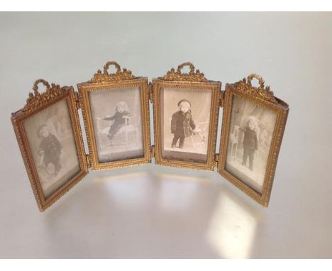 A French gilt-metal quadtych folding photograph frame, each rectangular aperture beneath a floral wreath surmount, enclosing 