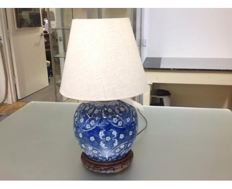 A Chinese style blue and white porcelain table lamp, decorated with flowering branches, on an integral wooden stand. Height e