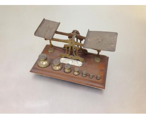 A set of early 20th century brass postal scales, the mahogany base with a full set of weights, bearing an ivorine plaque "Inl