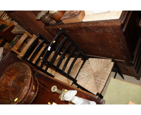 A pair of ebonised rush seated ladder back chairs; and a pair of pine similar