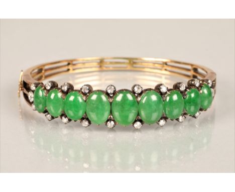 Ladies yellow metal stiff bangle set with nine oval cabochon jade stones, surrounded by twenty two small diamonds. Total weig