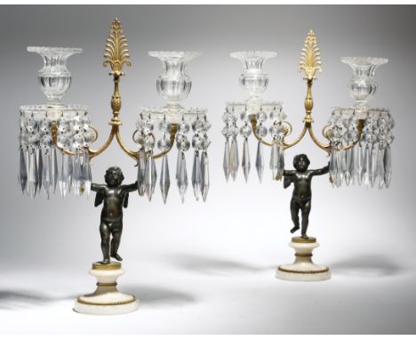 A pair of Regency gilt and patinated bronze figural twin-light candelabra, each modelled with a winged putto, standing on a w