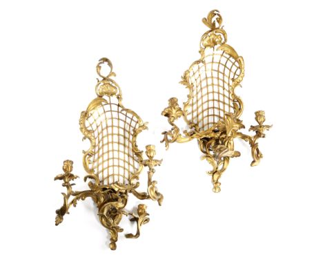 A pair of French ormolu three-light wall appliques in Louis XV style, each with a leaf, scroll and rocaille frame with a latt