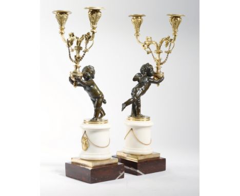 A pair of French early 19th century gilt and patinated bronze figural twin-light candelabra, each with a cherub holding an ur