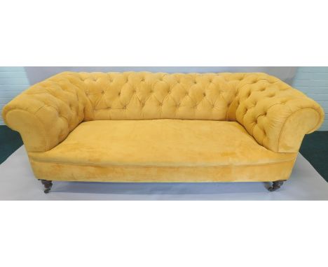 A Victorian chesterfield sofa, upholstered in yellow fabric, on turned legs with brass castors, 185cm wide