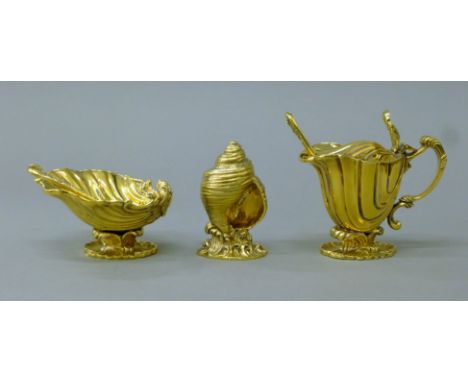 A silver gilt cruet set comprising a salt, a mustard pot and a pepper castor and two spoons, each of shell form. The mustard 