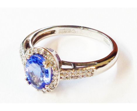 A platinum ring, set with central oval tanzanite within a diamond border with further small diamonds to shoulders - size P - 