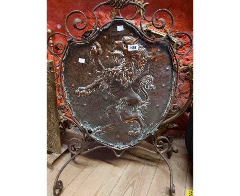 An Arts &amp; Crafts Movement fire screen with central copper shield shaped panel decorated with a repousse lion rampant with