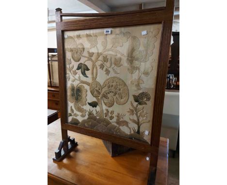 An Arts &amp; Crafts stained oak framed fire screen with crewel work panel under glass depicting deer beneath a tree, set on 